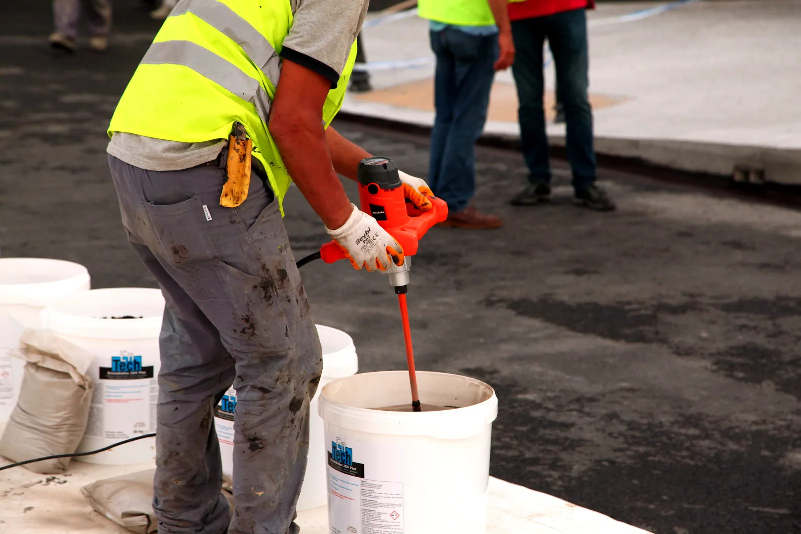 A worker in safety gear mixes material at a construction site using a mud mixer.