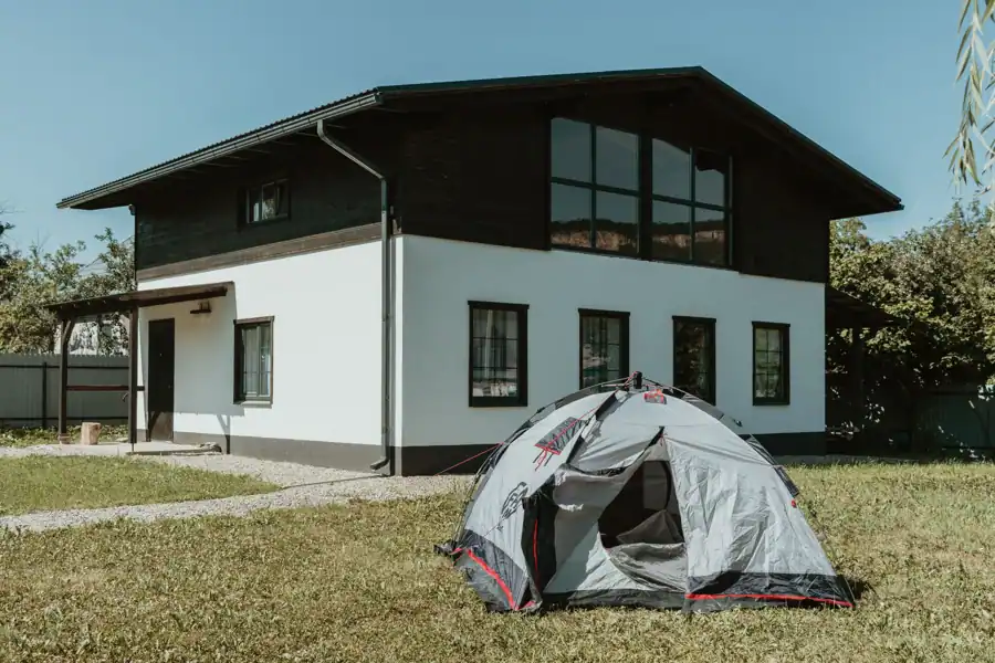 A modern two-story house with a pitched roof and a camping tent in the grassy garden.